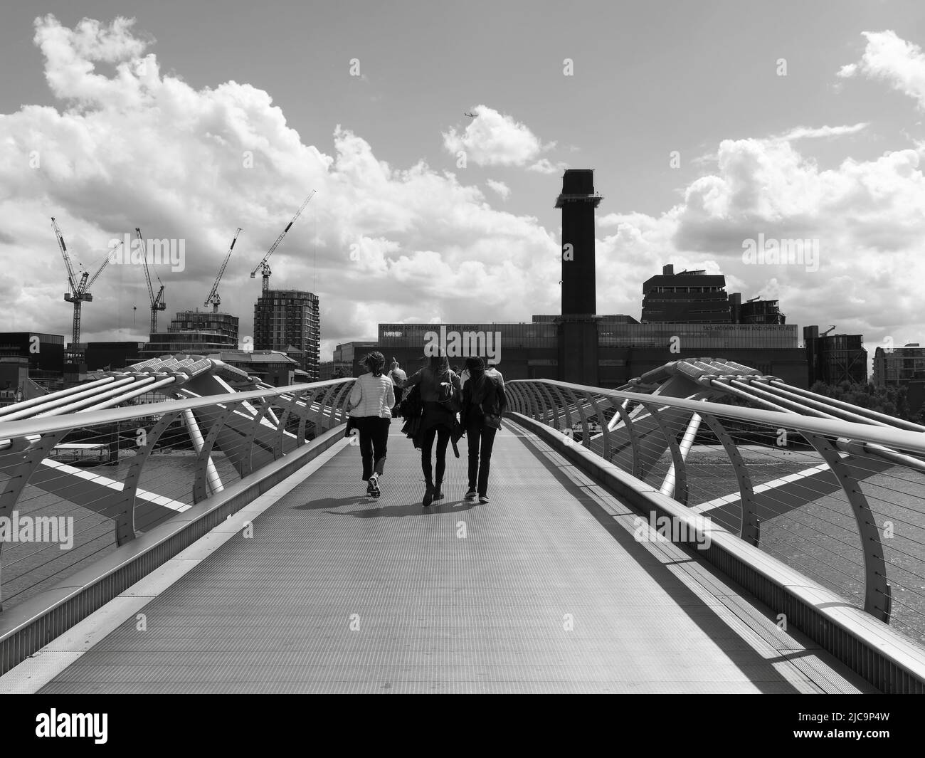 London, Großraum London, England, Juni 08 2022: Monochrom. Touristen sehen Sehenswürdigkeiten auf der Millennium Bridge mit Tate Modern Gebäude im Hintergrund. Stockfoto