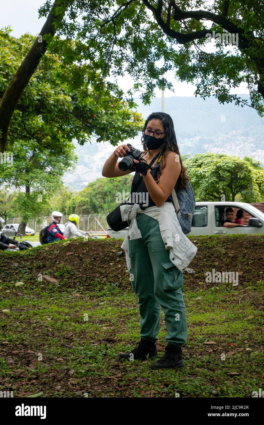 Medellin, Antioquia, Kolumbien - Februar 19 2022: Kolumbianerin mit langen braunen Haaren hält ihre Kamera in einem schönen Garten nahe der Straße Stockfoto