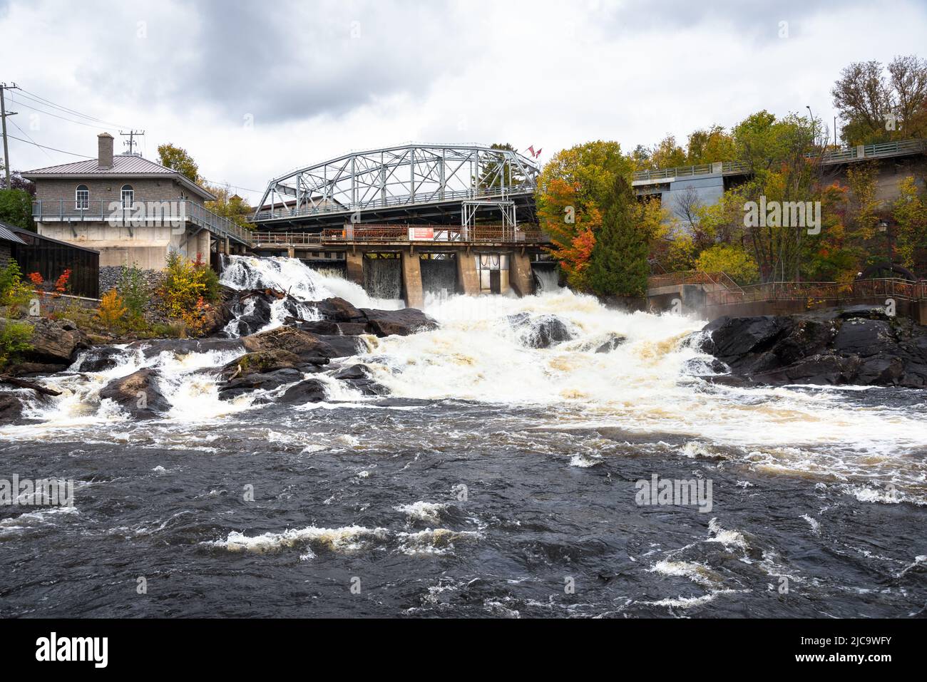 An einem bewölkten Herbsttag fließendes Wasser über den Gipfel eines kleinen Staudamms A entlang eines Flusses Stockfoto