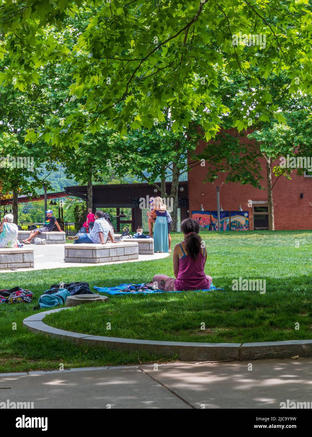 ASHEVILLE, NC, USA-5 JUNE 2022: Junge Frau meditiert auf dem Pack Square, andere Menschen in der Ferne. Stockfoto