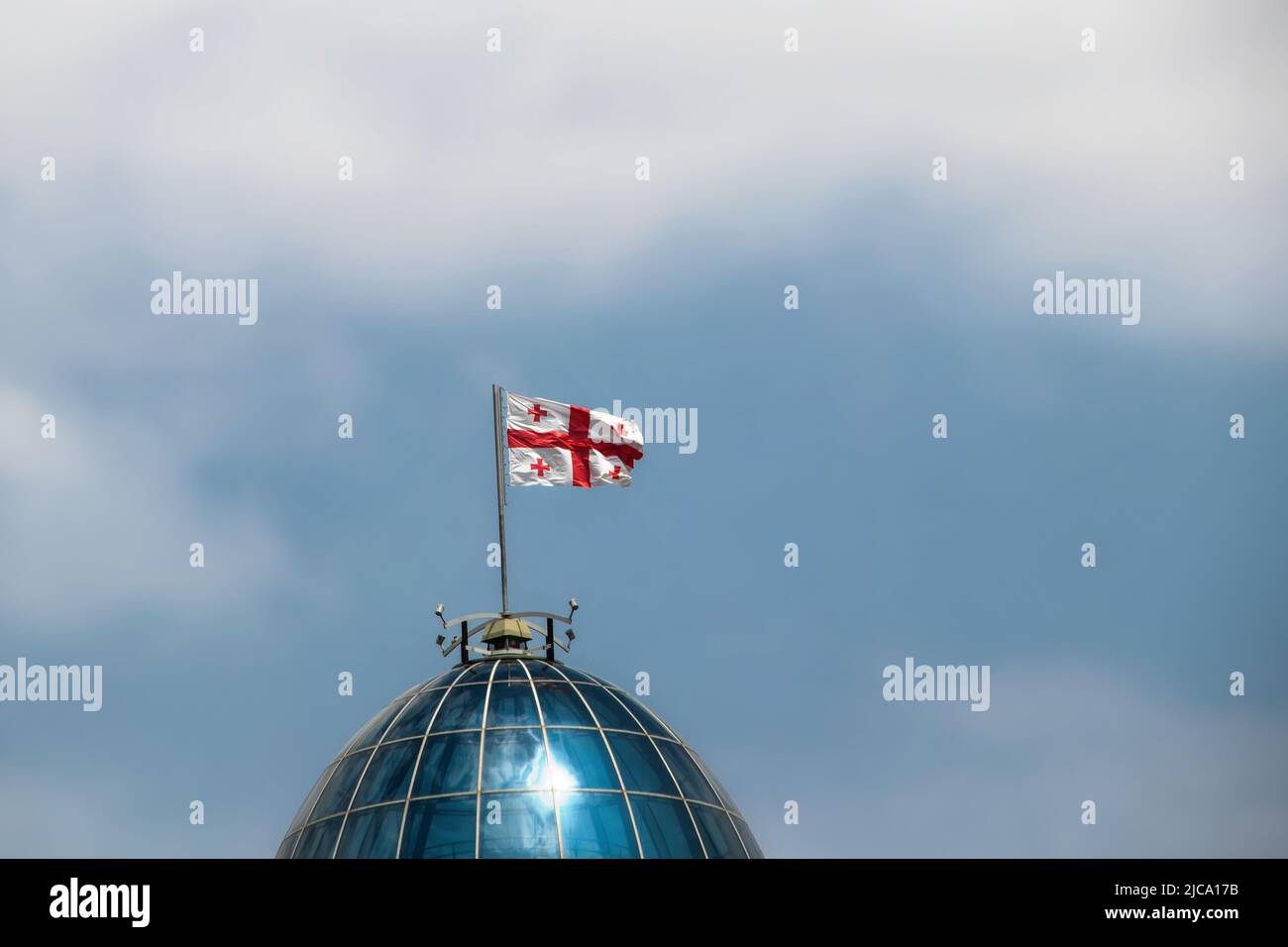 Nahaufnahme der Flagge der Republik Georgien weht im Wind auf der Kuppel der Hauptstadt in Tiflis mit einem blauen bewölkten Himmel dahinter - Raum für Kopie Stockfoto
