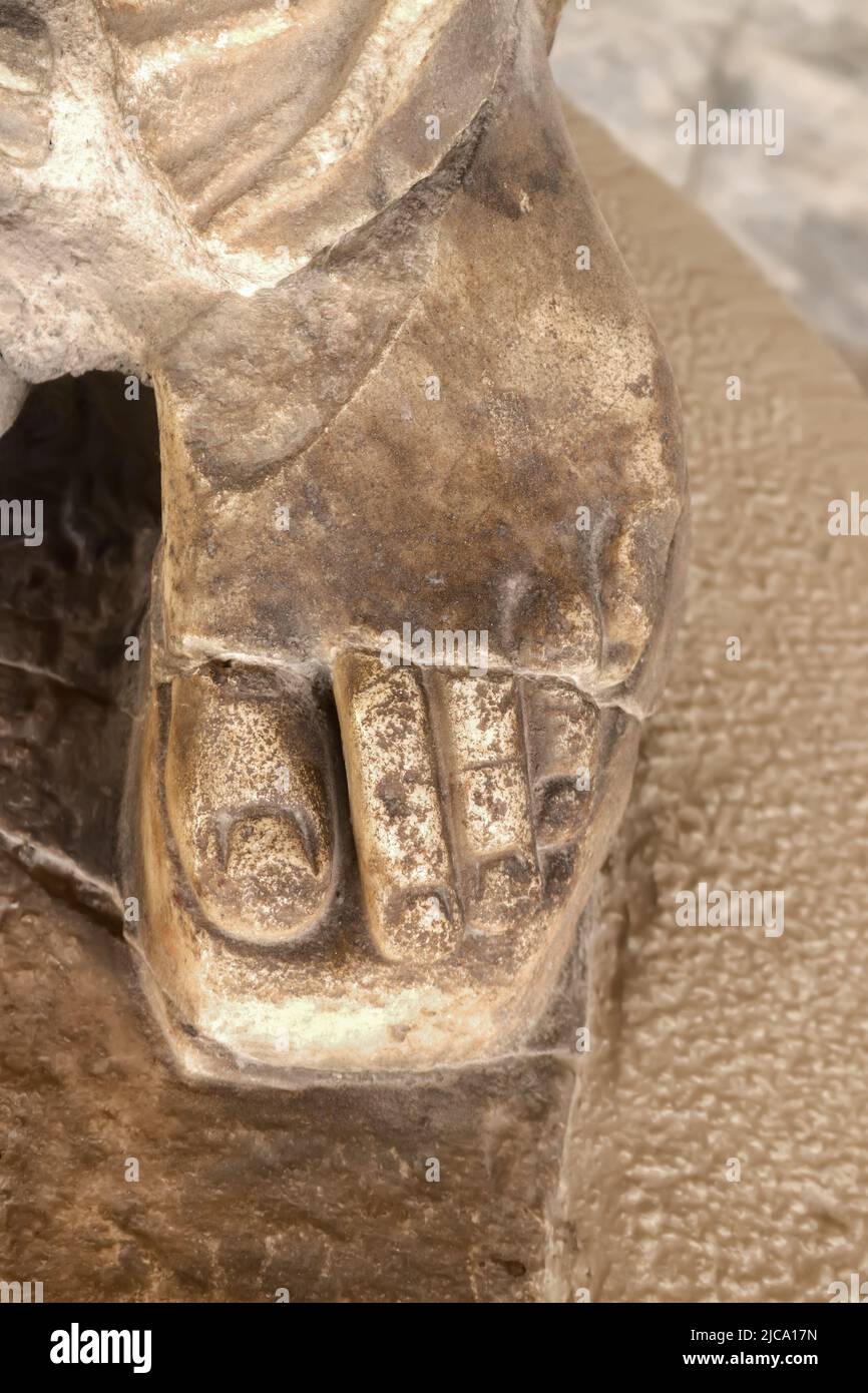 Nahaufnahme des Fußes in Sandale mit Zehen, die eine antike griechische Statue zeigen - körniger, geschnitzter Marmor vor einem verschwommenen Hintergrund Stockfoto