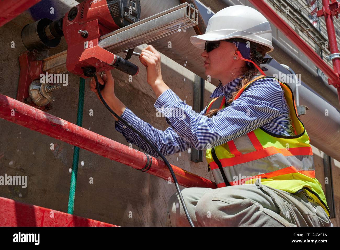 Ein weiblicher Bauarbeiter-Kern bohrt in eine Betonhalterung ein Stockfoto