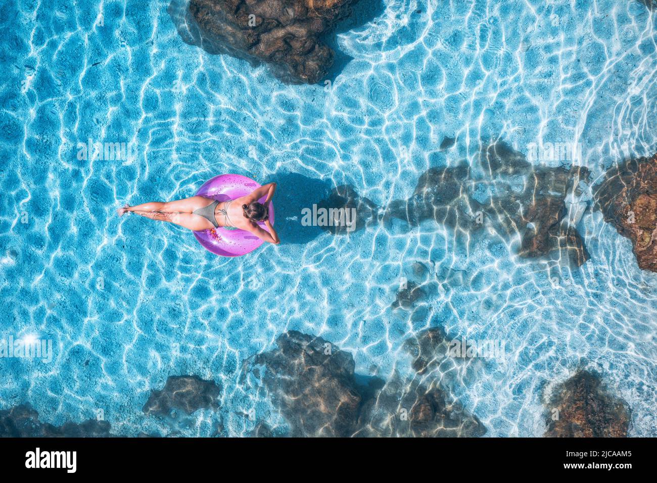 Luftaufnahme einer jungen Frau, die mit einem Schwimmring im blauen Meer schwimmt Stockfoto