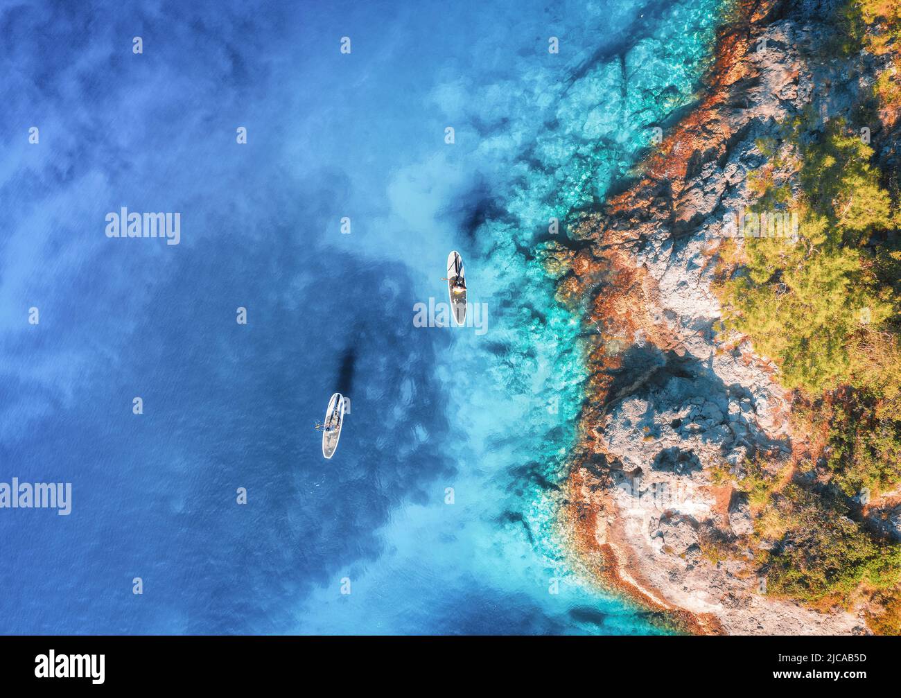 Luftaufnahme von Menschen auf schwimmenden Schautafeln auf blauem Meer, Felsen Stockfoto