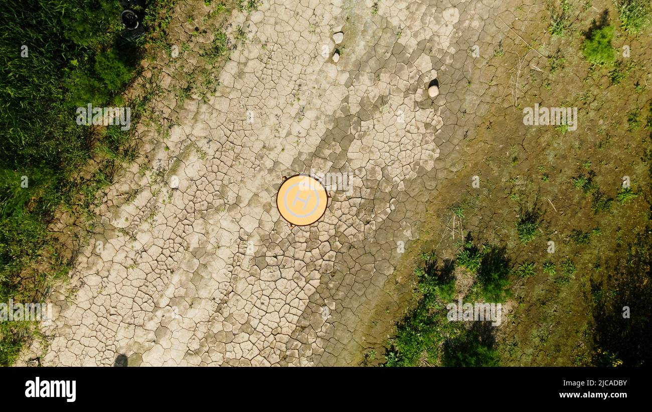 Der Quadcopter-Landeplatz befindet sich auf dem Boden. Der Boden ist mit rissiger Kruste bedeckt. Luftaufnahmen. Stockfoto