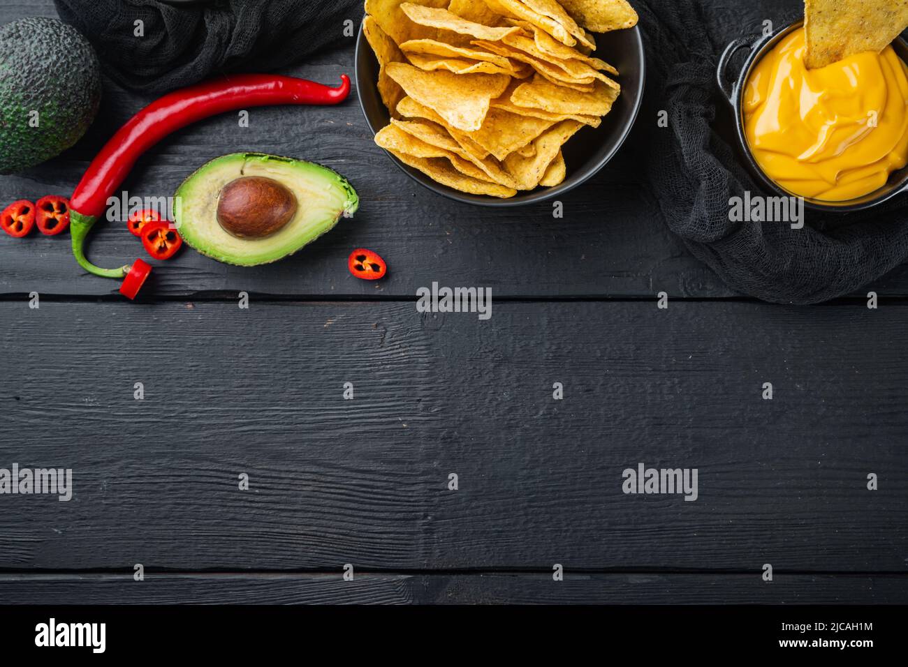 Dreieckiger gelber Maistortilla-Chip mit Soße, auf schwarzem Holzhintergrund, Draufsicht oder flacher Lay mit Kopierraum für Text Stockfoto