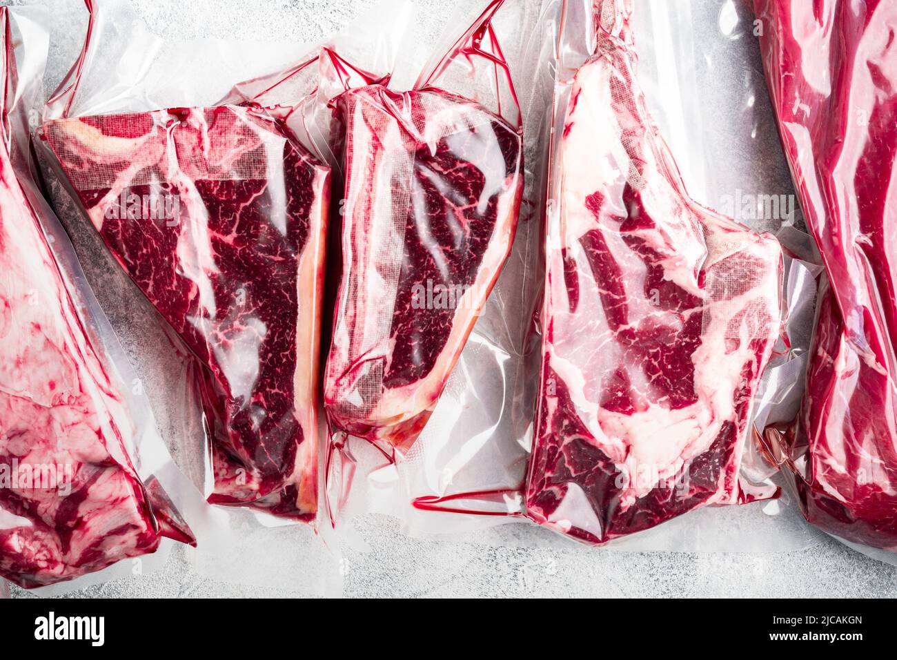 Rindersteak Vakuum, Tomahawk, t Bone, Clubsteak, Rib Eye und Filet Schnitte, auf grauem Stein Hintergrund, Draufsicht flach gelegen Stockfoto