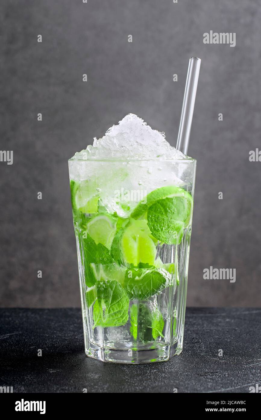 Frischer Mojito aus Zitrusfrüchten und grünen Minzblättern auf dunklem Grund. Glas mit köstlichem alkoholfreiem Getränk mit zerkleinertem Eis und Stroh Stockfoto