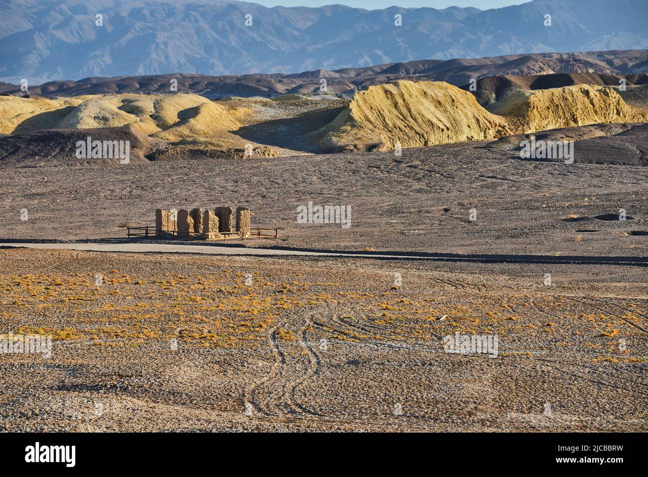 Offene Wüstenlandschaft mit Reifenspuren und alter Steinstruktur durch Berge Stockfoto