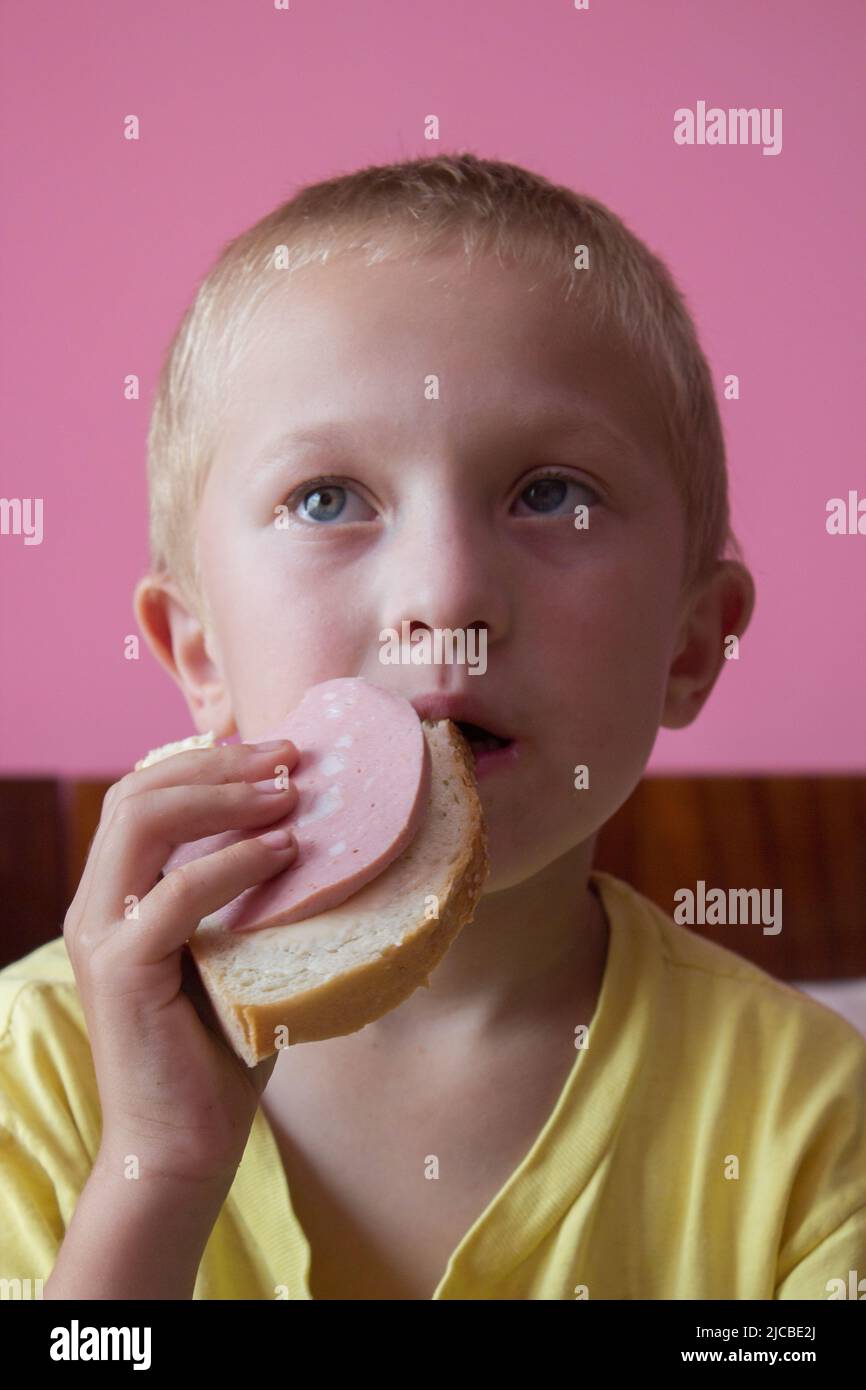 Überrascht Junge essen gekochte Wurst mit Brot Stockfoto