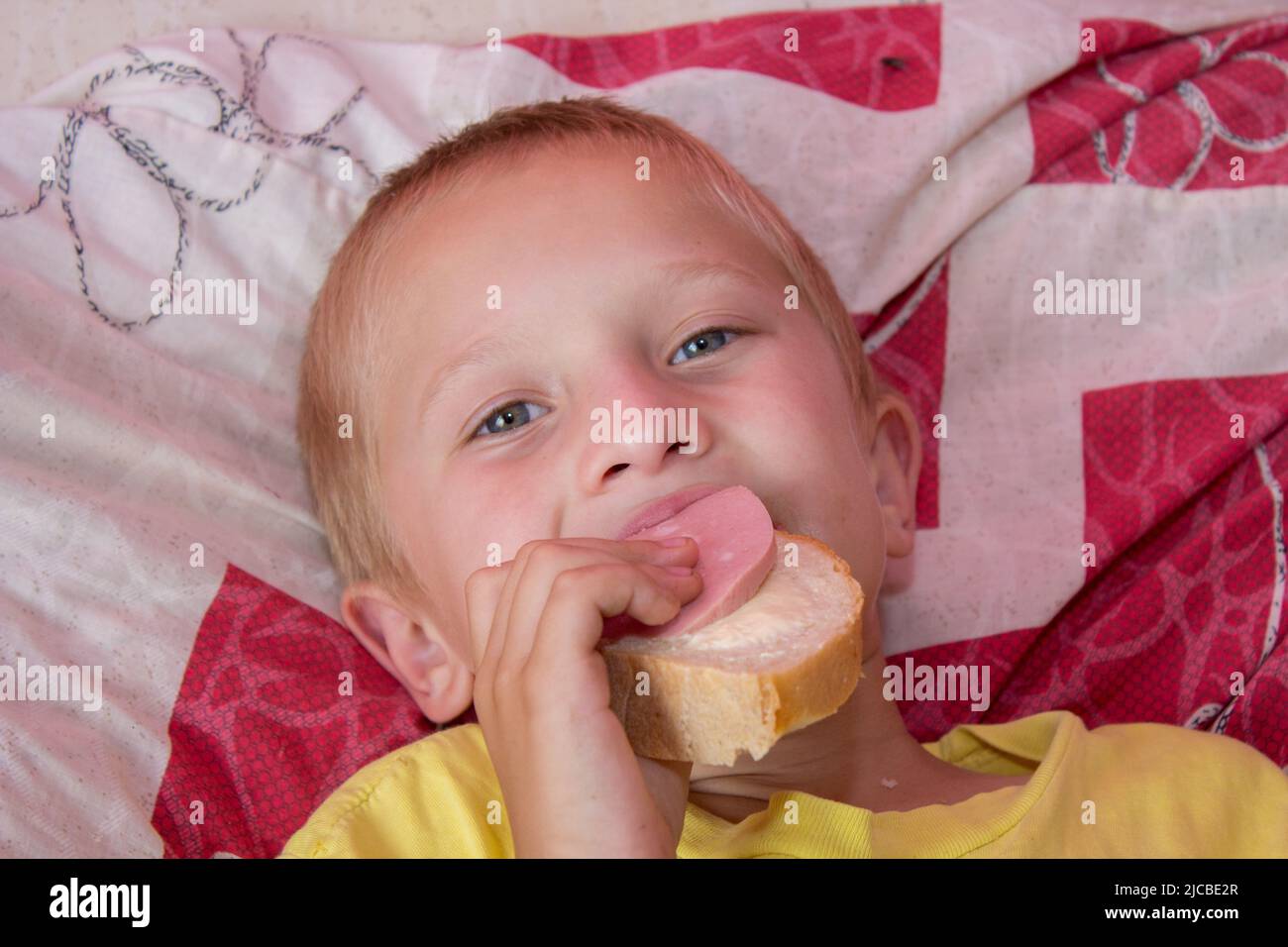Junge liegt auf dem Bett und isst Sandwiches Stockfoto