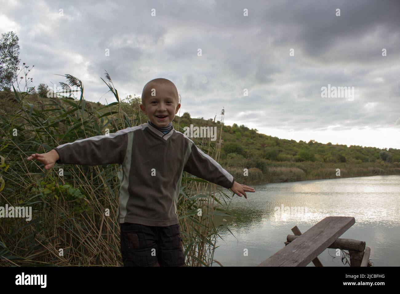 Die Hände auf der Seite des Jungen lachten im Herbst am Ufer des Sees Stockfoto