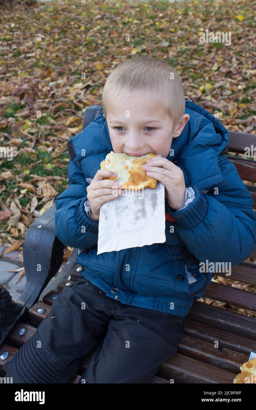 Junge essen Pasties im Herbst auf der Bank Stockfoto