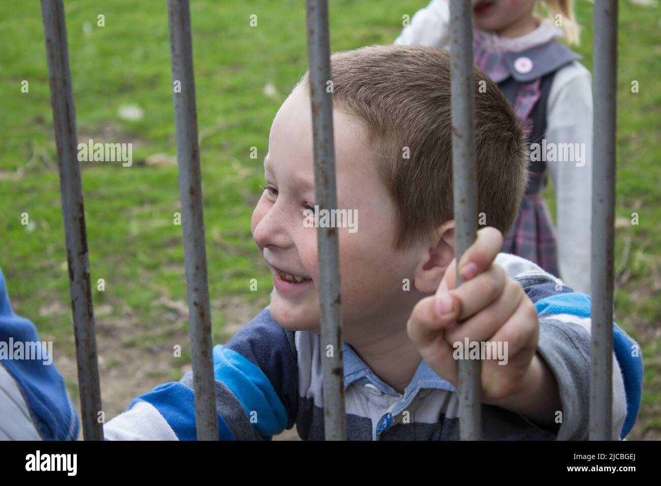 Junge schaut durch einen Metallzaun und lächelt Stockfoto