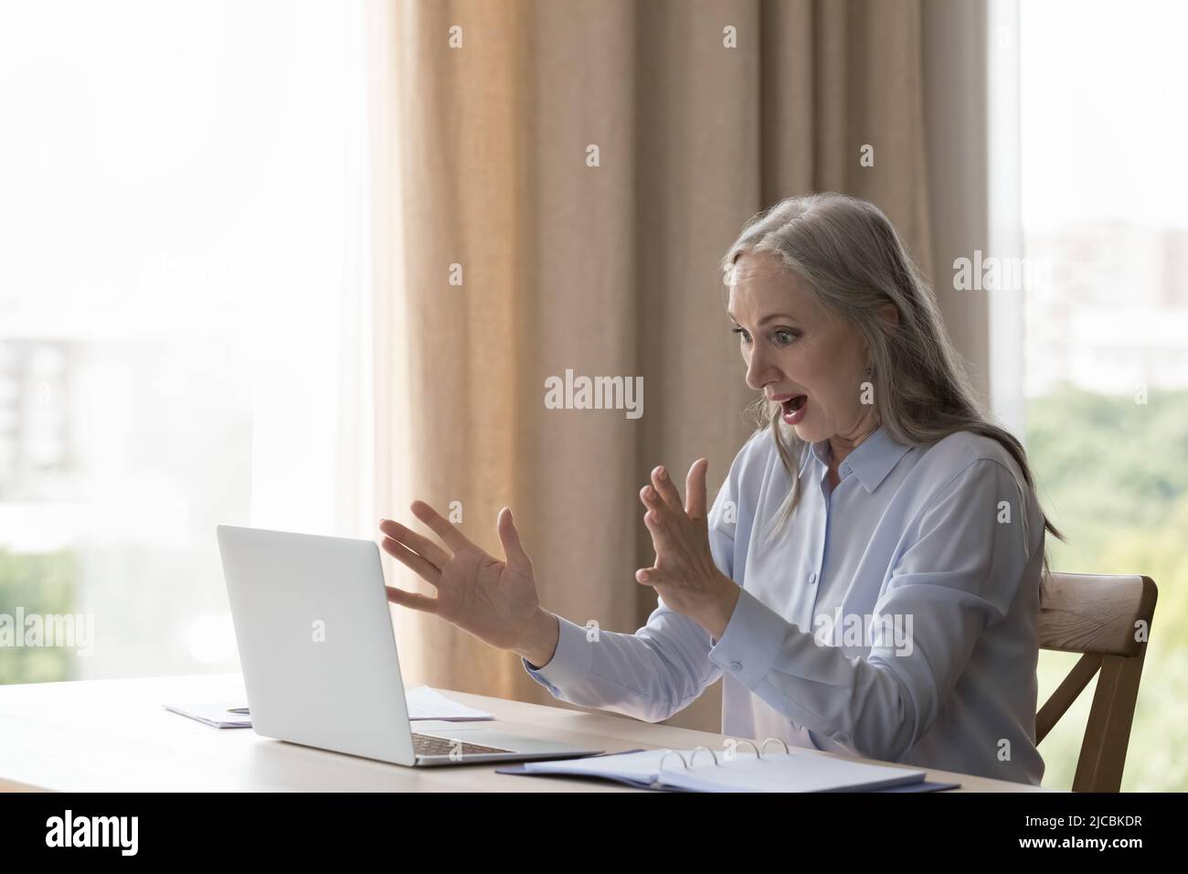 Ältere Geschäftsfrau mit offenem Mund beim Laptop-Bildschirm fühlt sich schockiert Stockfoto