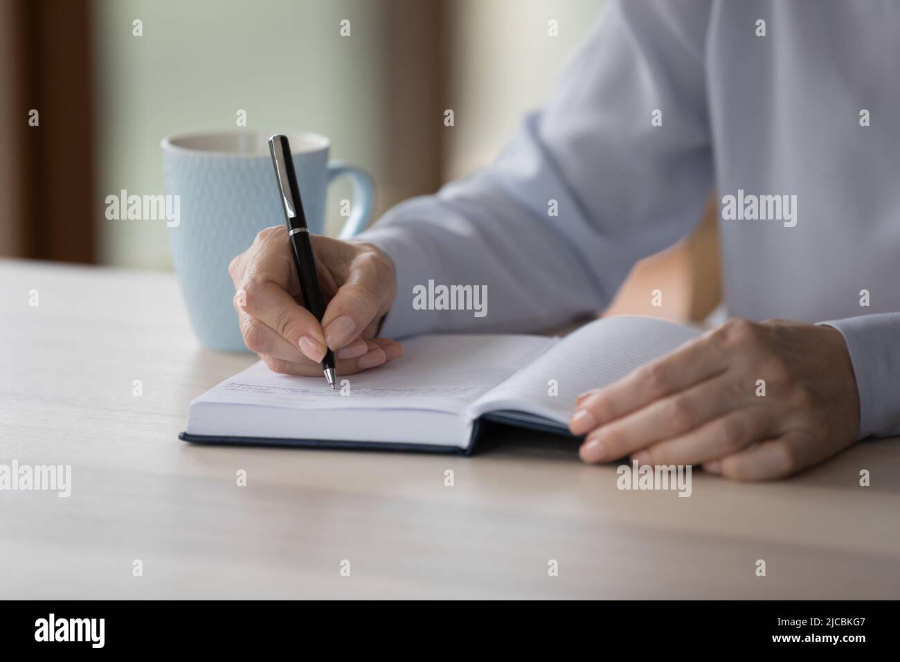 Nahaufnahme einer älteren Frau, die in einem Papierplaner Notizen schreibt Stockfoto