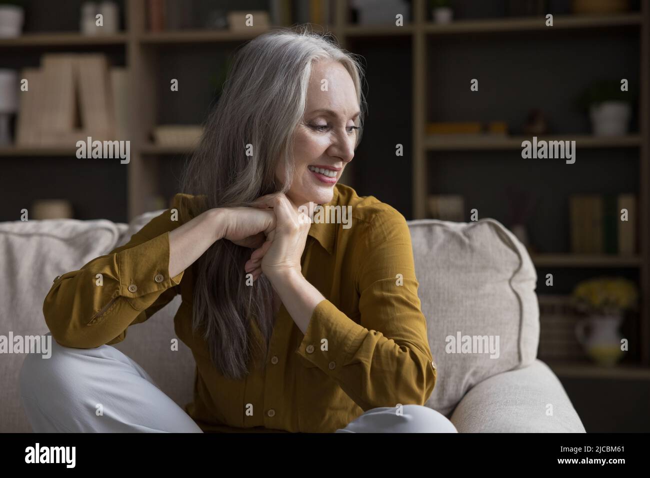 Ruhige, schöne Frau mittleren Alters, die sich auf einem gemütlichen Sofa entspannt Stockfoto