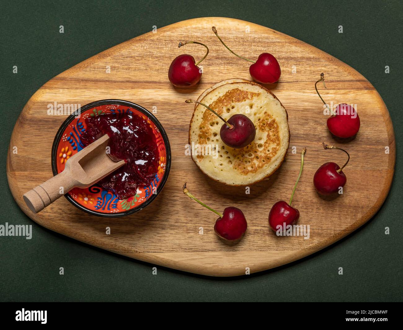 Kirschmarmelade, rote Kirschen und Pfannkuchen auf einem Holzschneidebrett Stockfoto