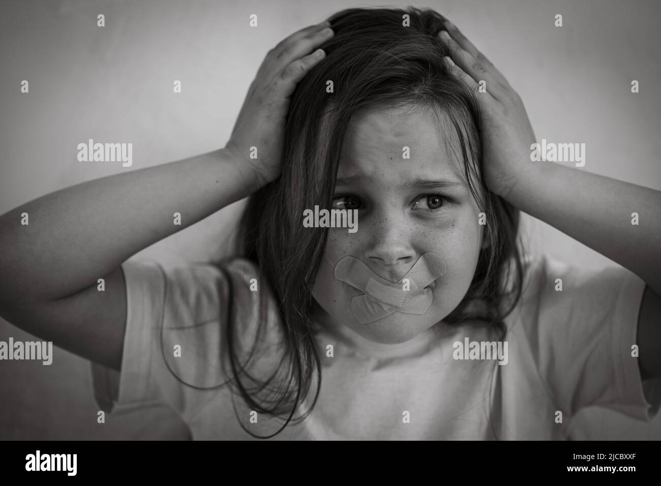 Schwarz-weiß Porträt von kleinen in Panik geratenen Mädchen mit langen dunklen Haaren packenden Kopf. Mund mit medizinischen Pflaster verschlossen. Stockfoto