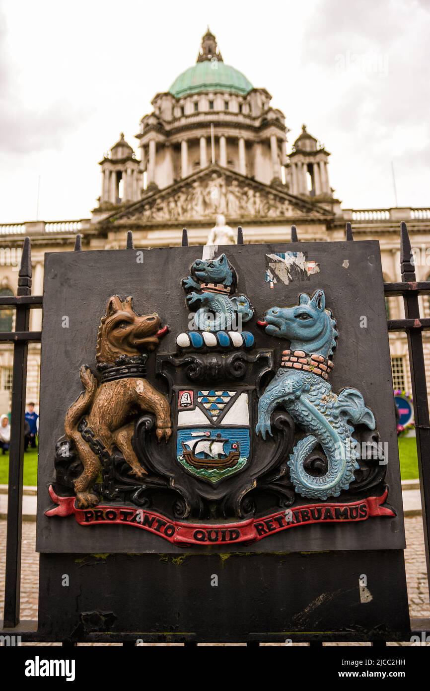 Belfast, Vereinigtes Königreich - 21. Mai 2022: Wappen als Relief auf einem eisernen Tor und im Hintergrund die Kuppel des Rathauses in Belfast, Northern IRE Stockfoto