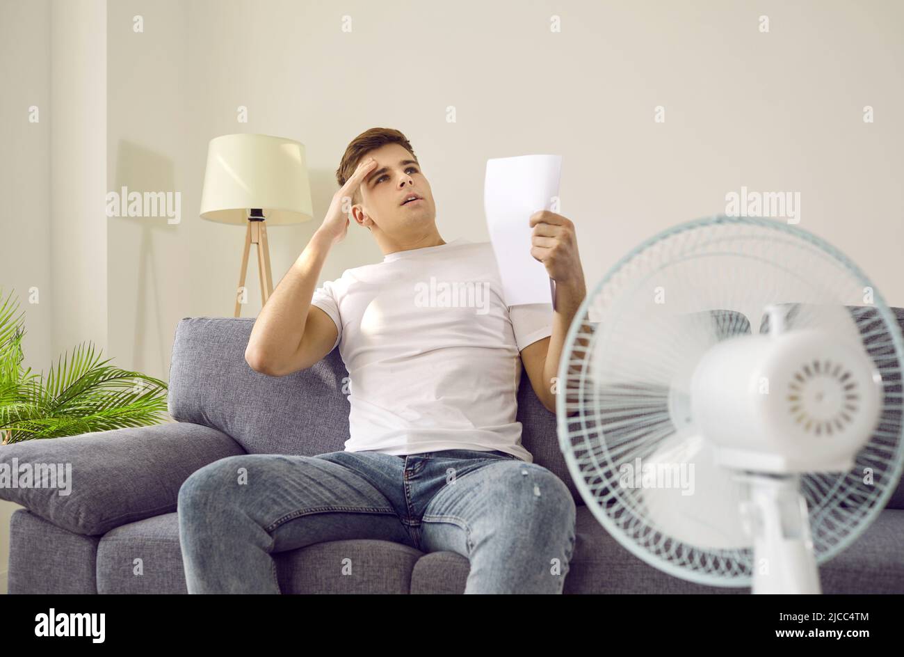 Verschwitzter Mann fühlt sich schlecht wegen der schrecklichen Hitze sitzen zu Hause vor einem Ventilator während der heißen Sommertage Stockfoto