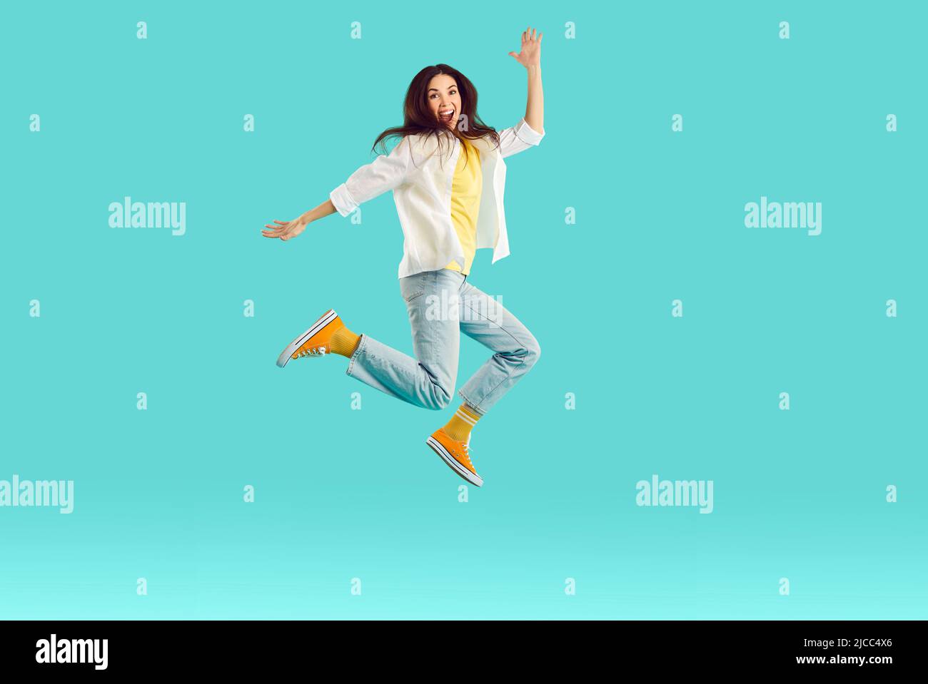 Fröhlich aufgeregt junge Frau mit Spaß und Herumtollen springen hoch auf hellblauem Hintergrund. Stockfoto