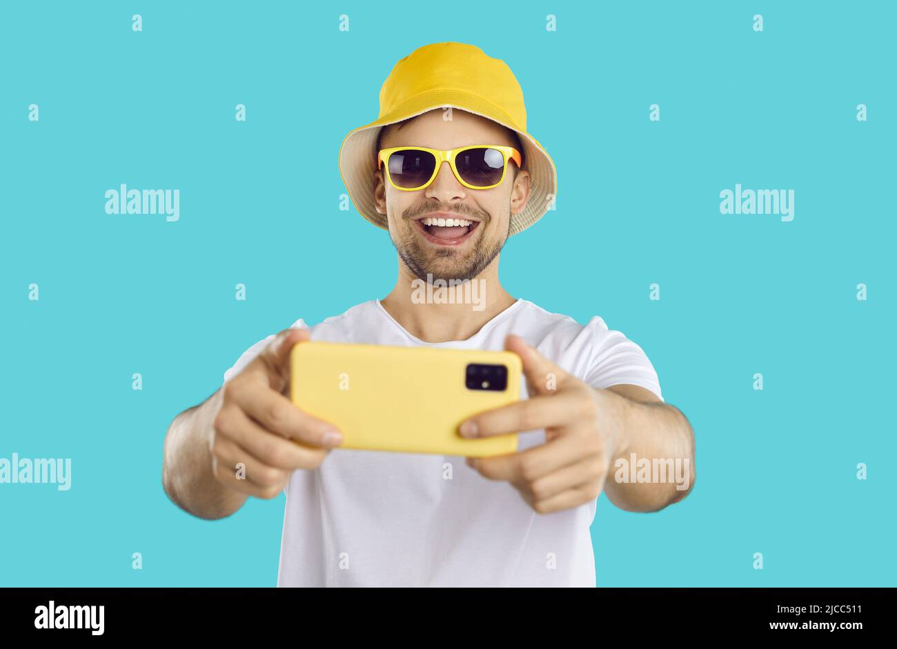 Fröhlicher, sorgloser Kerl, der Selfie auf einem Mobiltelefon auf hellblauem Hintergrund macht. Stockfoto