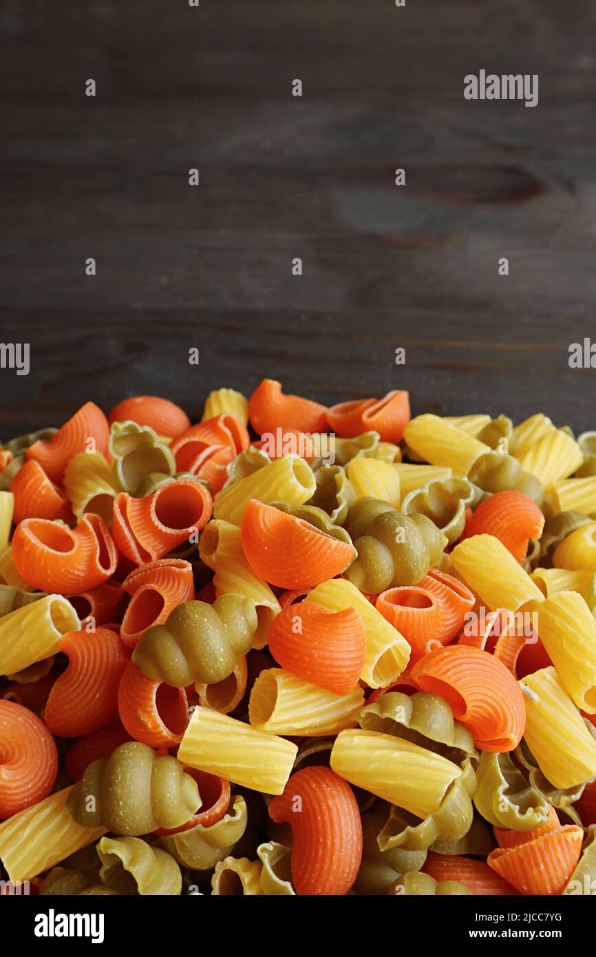 Stapel von verschiedenen Formen dreifarbige ungekochte Vegeroni Pasta auf schwarzem Holzhintergrund Stockfoto