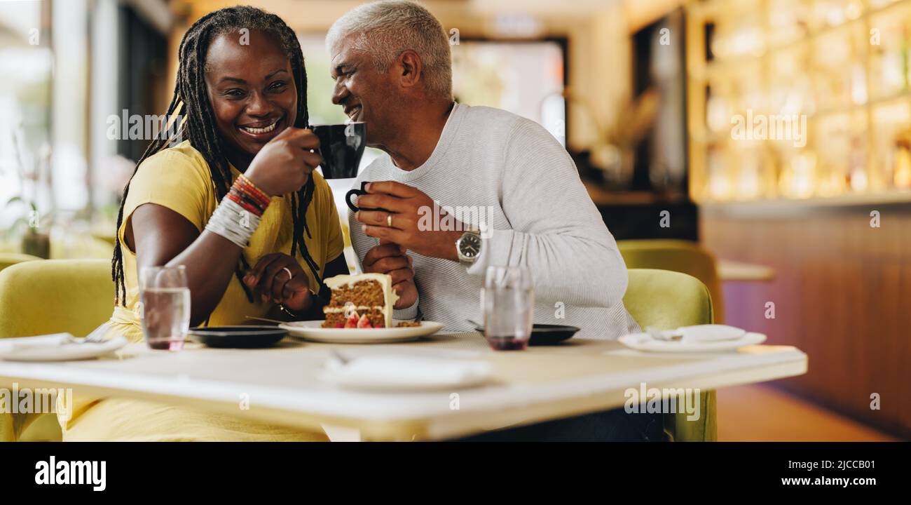 Ein glückliches Ehepaar, das fröhlich lächelt, während es in einem Café zusammen isst. Sorgenfreies Seniorenpaar, das eine gute Zeit in einem Restaurant hat. Reifes Coupl Stockfoto