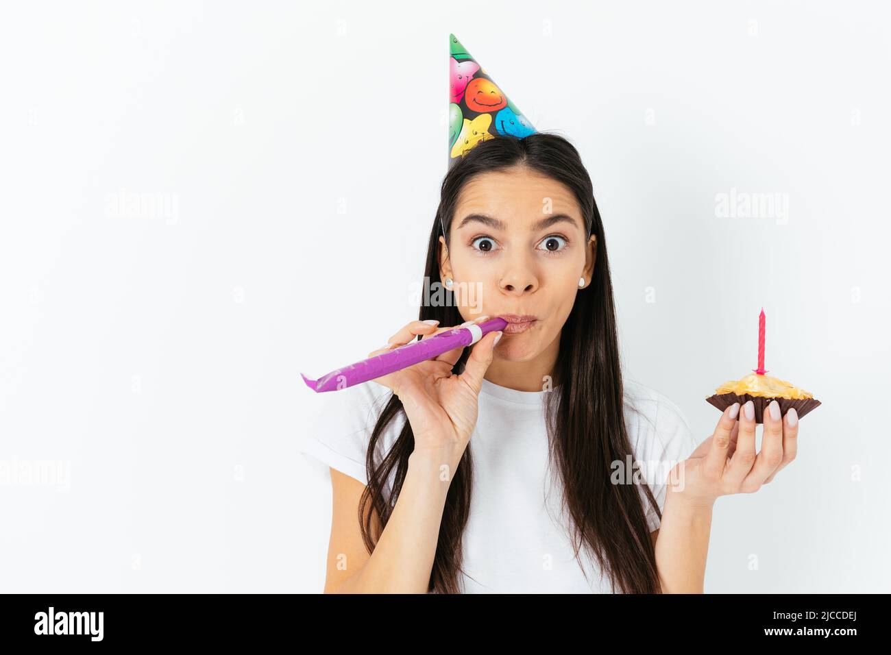 Junge Frau feiert überrascht Schläge in Kazoo hält Geburtstagskuchen, weißen Studio Hintergrund Stockfoto