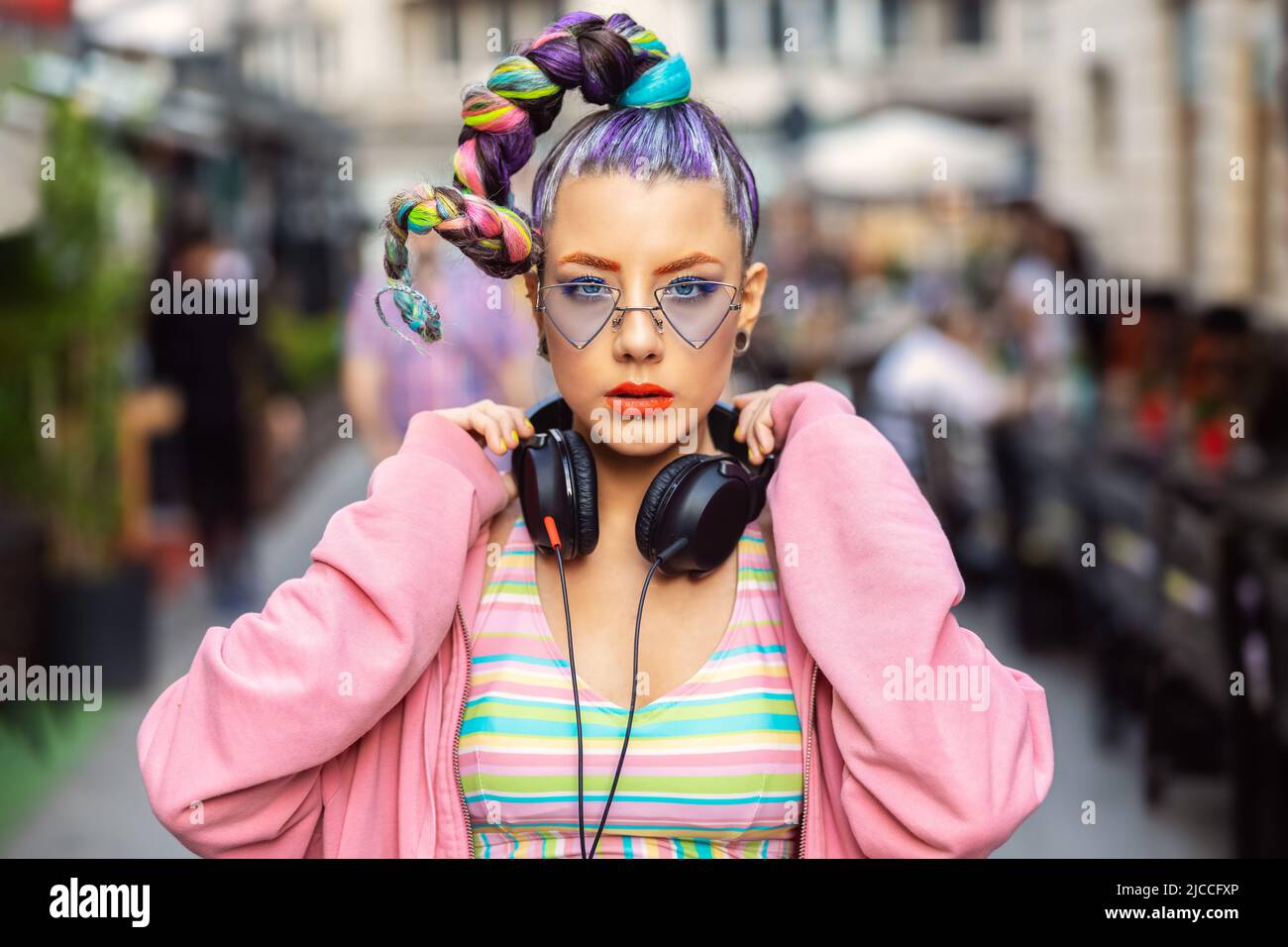 Coole, flippige junge Frau mit trendigen Brillen, die Musik auf Kopfhörern im Freien hören Stockfoto