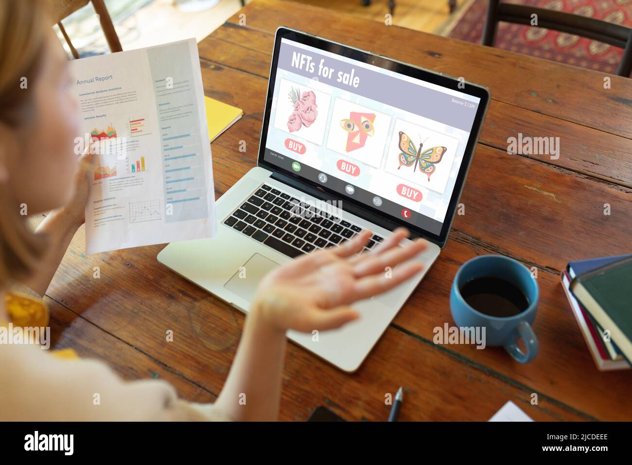 Kaukasische Geschäftsfrau, die einen Bericht hält, der nft über einen Laptop auf dem Tisch im Café analysiert Stockfoto