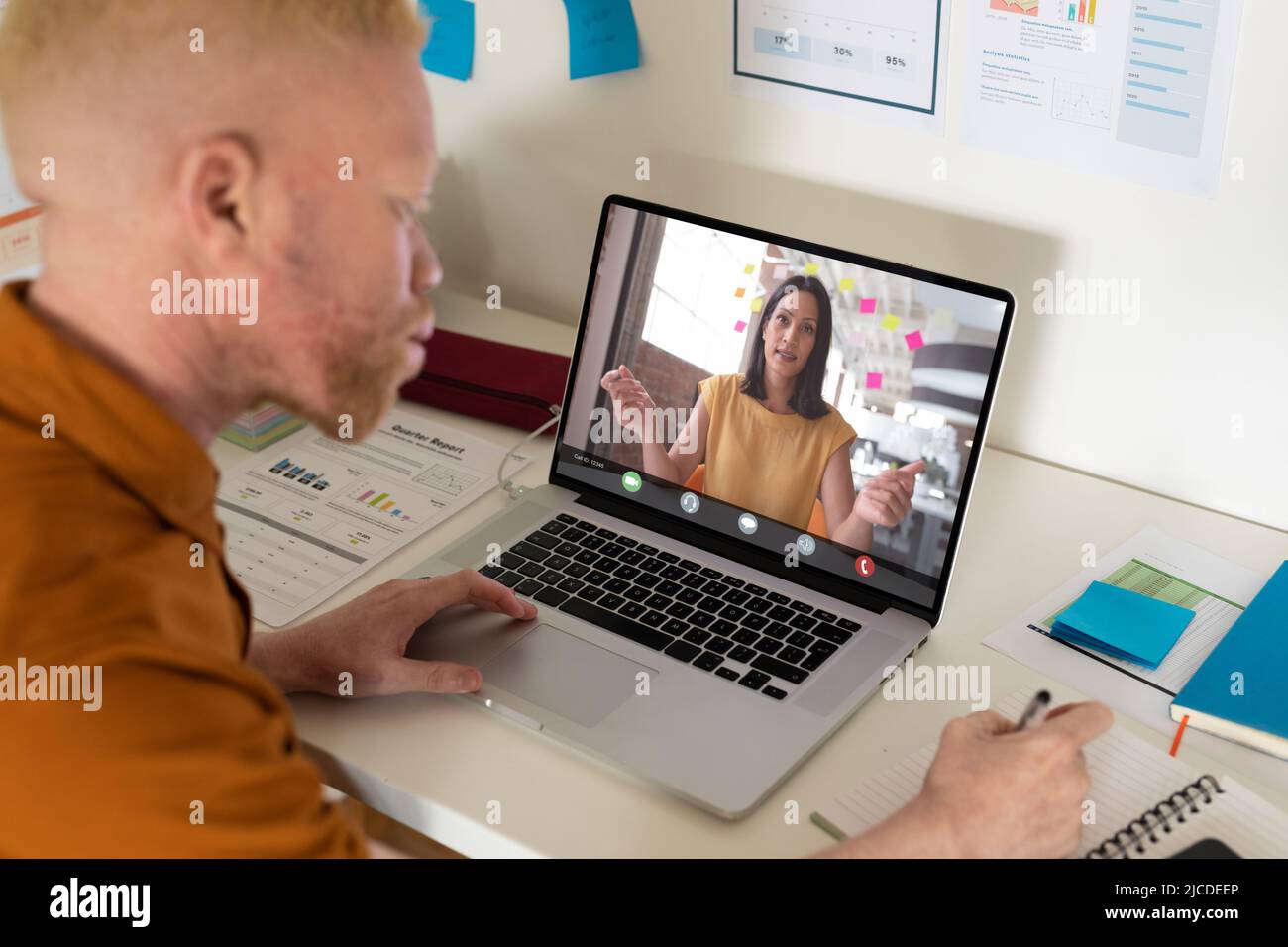 afroamerikanischer Albino-Geschäftsmann, der im Tagebuch schreibt, während er online mit einem Mitarbeiter auf dem Laptop diskutiert Stockfoto