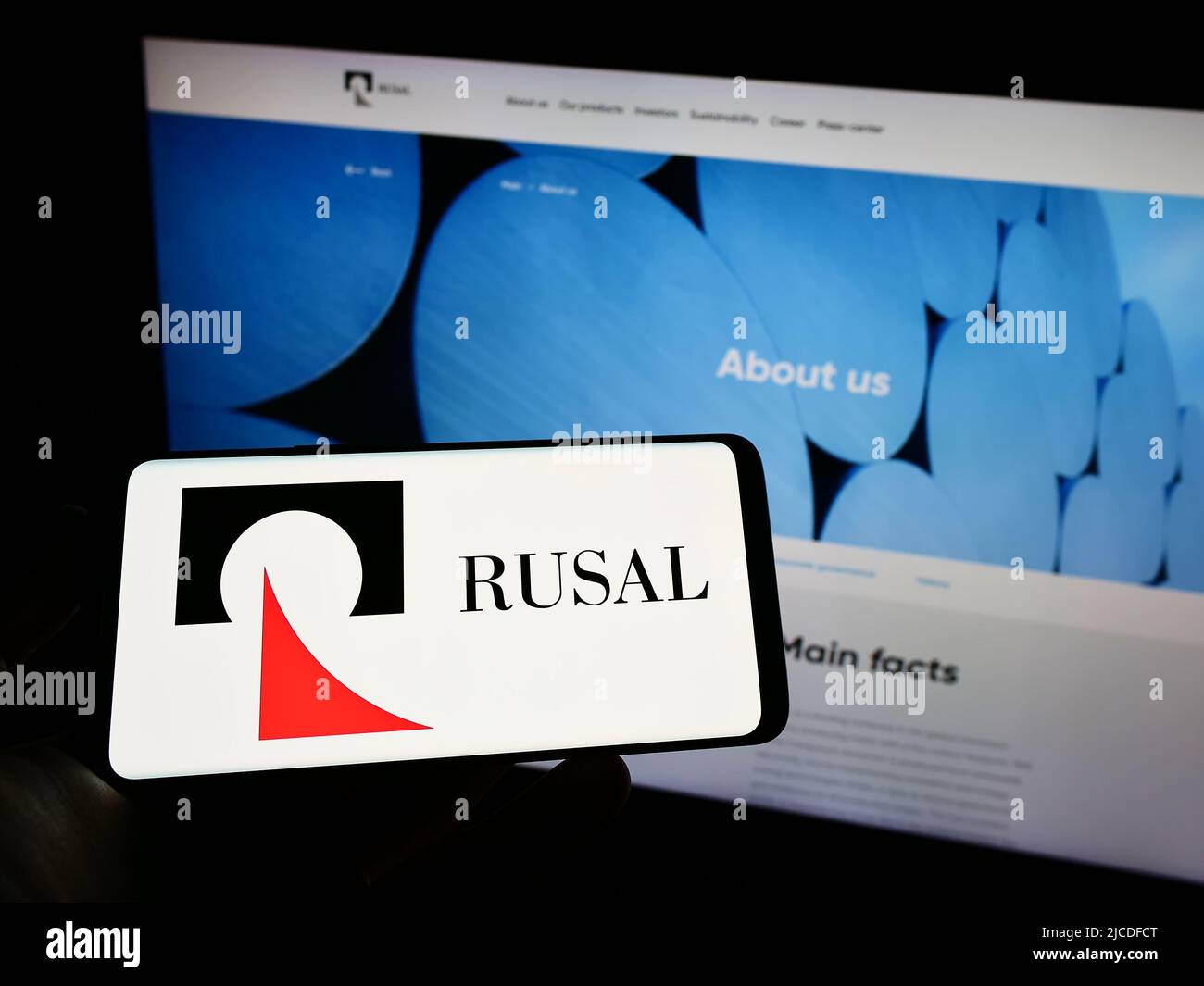 Person, die das Mobiltelefon mit dem Logo des russischen Unternehmens United Company RUSAL IPJSC auf dem Bildschirm vor der Webseite hält. Konzentrieren Sie sich auf die Telefonanzeige. Stockfoto