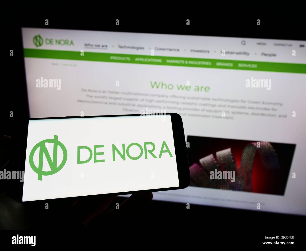 Person, die das Mobiltelefon mit dem Logo des italienischen Unternehmens Industrie De Nora Spa auf dem Bildschirm vor der Business-Webseite hält. Konzentrieren Sie sich auf die Telefonanzeige. Stockfoto