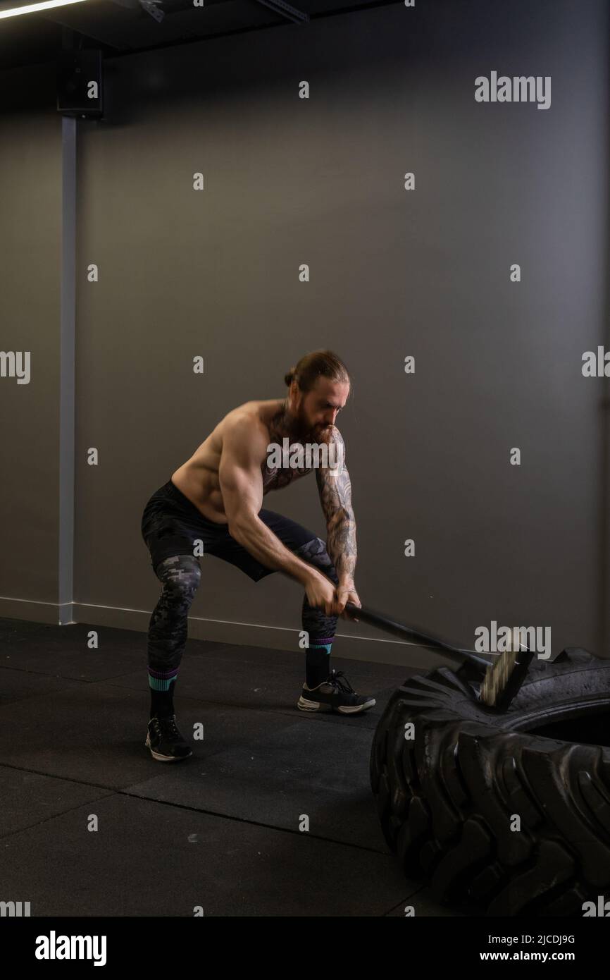 Reifen Schlitten Hammer muskulöses Rad Mann schlagen Übung Workout Kraft, Konzept Ausrüstung stark von sportlich aus Sportswear Konzentration, männlich Stockfoto