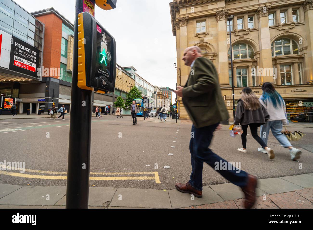 Fußgänger überqueren die Straße an der Market Street, Manchester. Eine Papageientaucher-Kreuzung zeigt den „grünen Mann“, wenn Menschen die Straße überqueren. England, Großbritannien Stockfoto