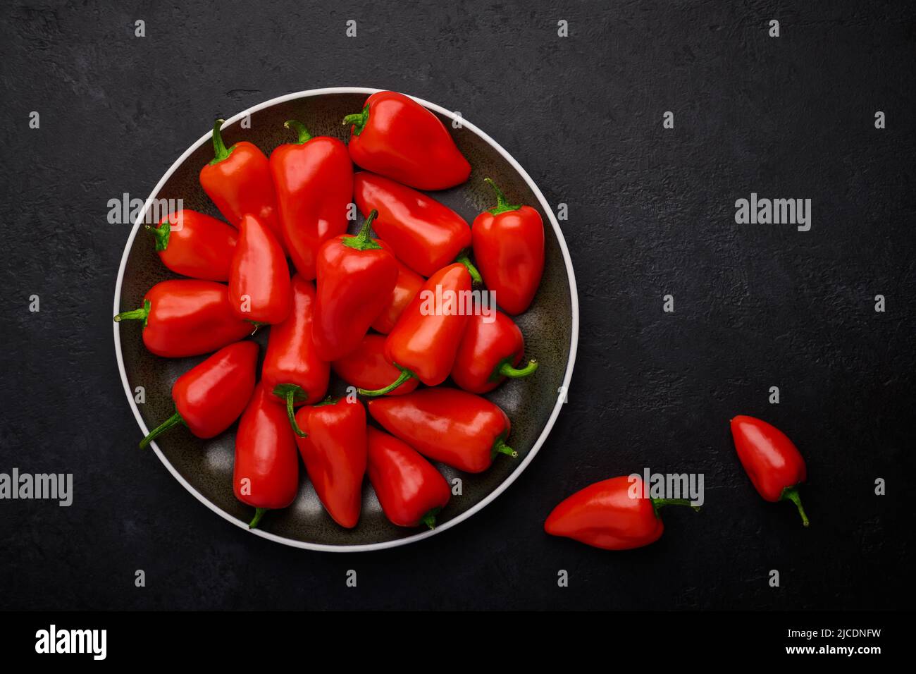 Kleine Schoten roter Paprika auf einem Teller, dunkler Schieferhintergrund Stockfoto