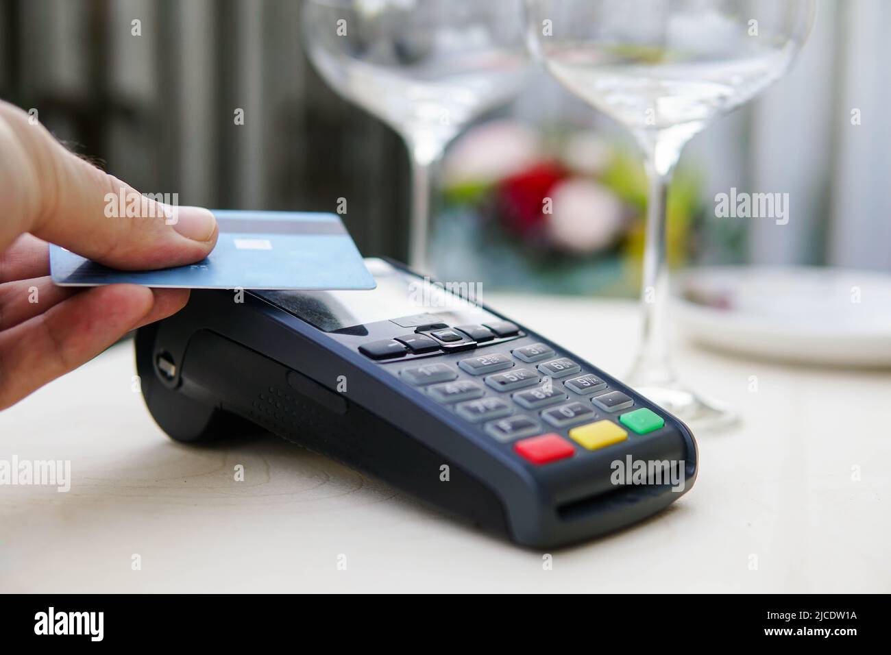 Zahlungsterminal mit Kreditkarte in der Nähe von Gläsern und Tellern auf dem Tisch im Restaurant. Konzept der elektronischen Finanzierung. Stockfoto