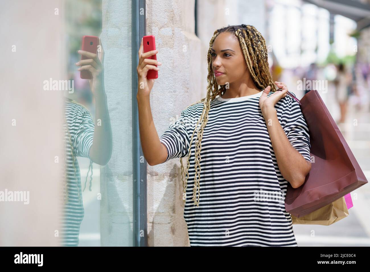 Die junge schwarze Frau fotografiert mit ihrem Smartphone ein Schaufenster in einer Einkaufsstraße. Stockfoto