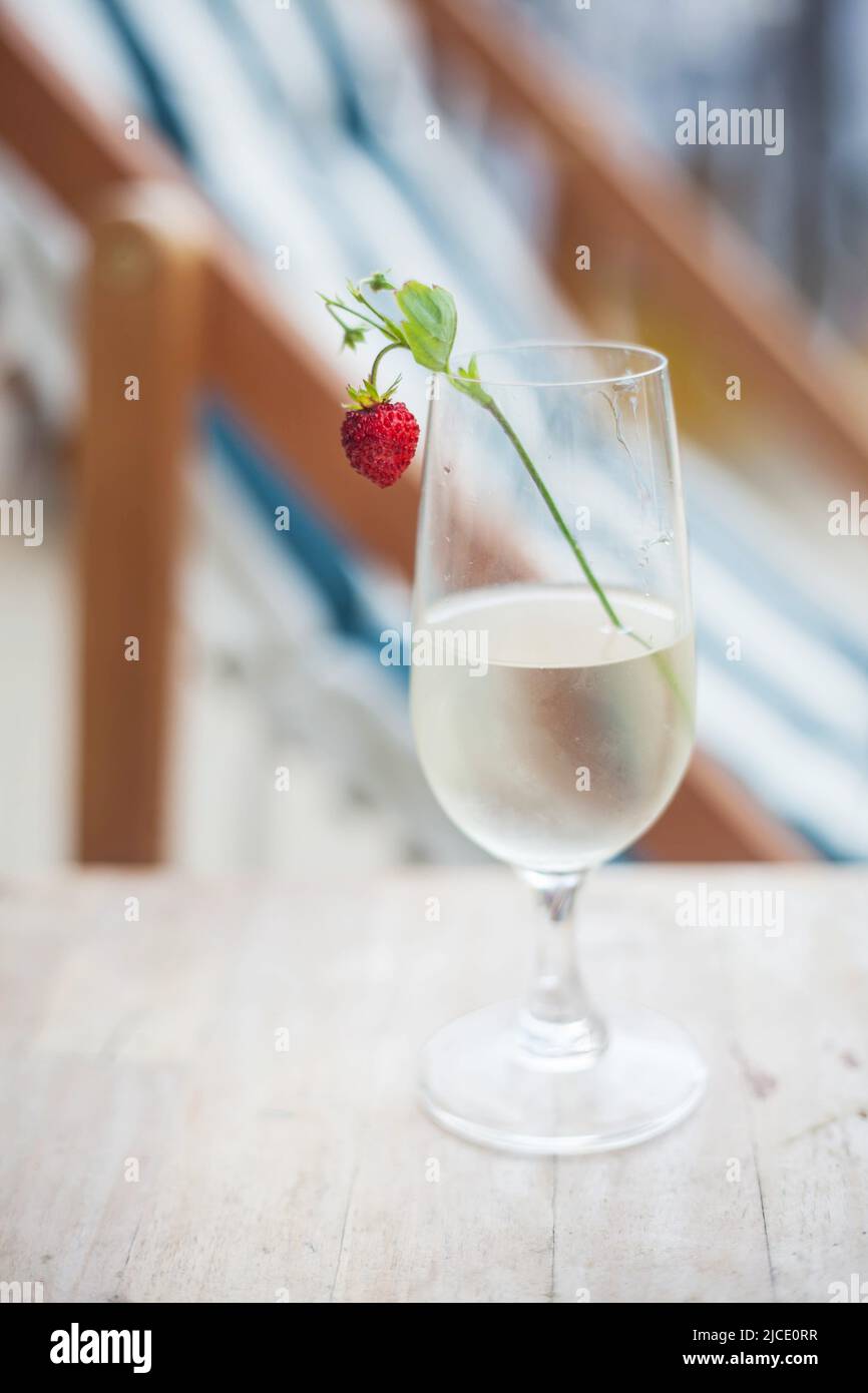 Ein Glas Weißwein mit Erdbeere auf dem Hintergrund eines Liegestuhls am Strand. Sommerzeit. Sommerliche Stimmung. Stockfoto