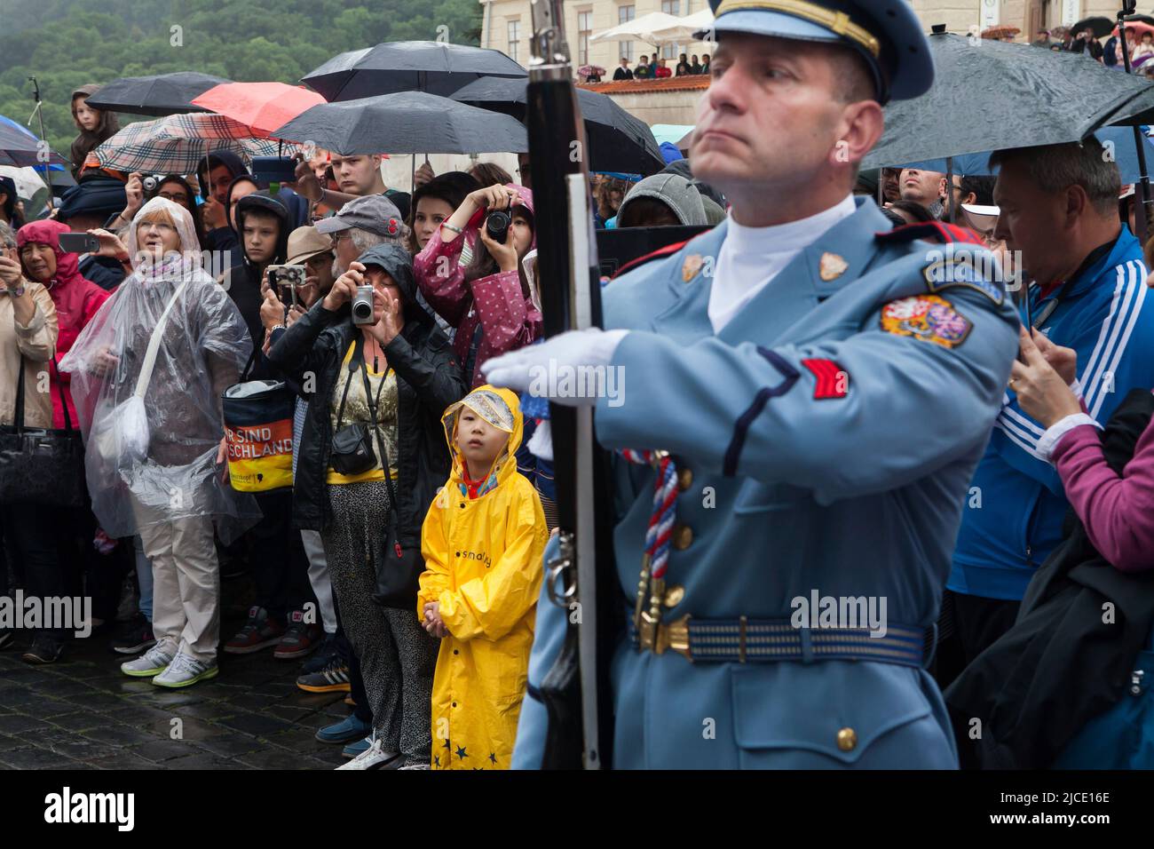 Touristen beobachten die Zeremonie der Wachablösung (Hradní Stráž) bei Regen vor der Prager Burg auf dem Hradčanské-Platz in Prag, Tschechische Republik. Stockfoto