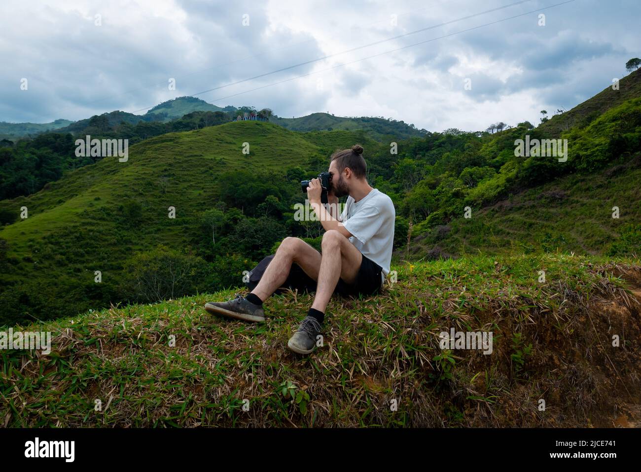 Weißer Mann, der Bilder von den grünen Bergen macht und im Gras sitzt Stockfoto
