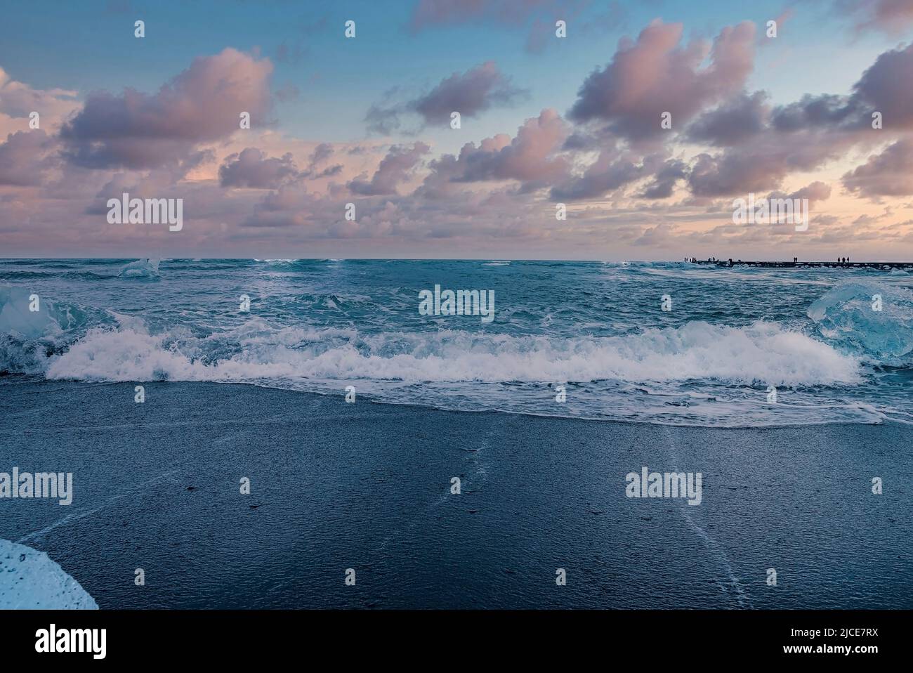 Szenischer Blick auf die Wellen am schwarzen Sandstrand von Diamond Beach gegen den Himmel bei Sonnenuntergang Stockfoto