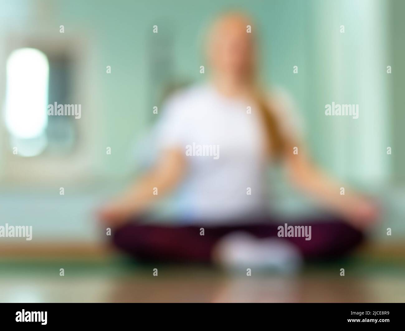 Verwischen Sie den Hintergrund mit einer gesunden Frau, die in der Halle Yoga praktiziert. Die Yoga-Anfängerin ist in Lotushaltung. Die Position erforderte Dehnung und Balance. Th Stockfoto