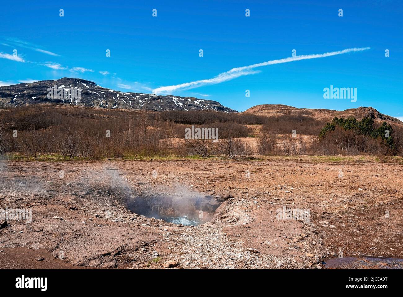 Rauch, der vom Strokkur-Geysir inmitten der Landschaft gegen den blauen Himmel aussendet Stockfoto