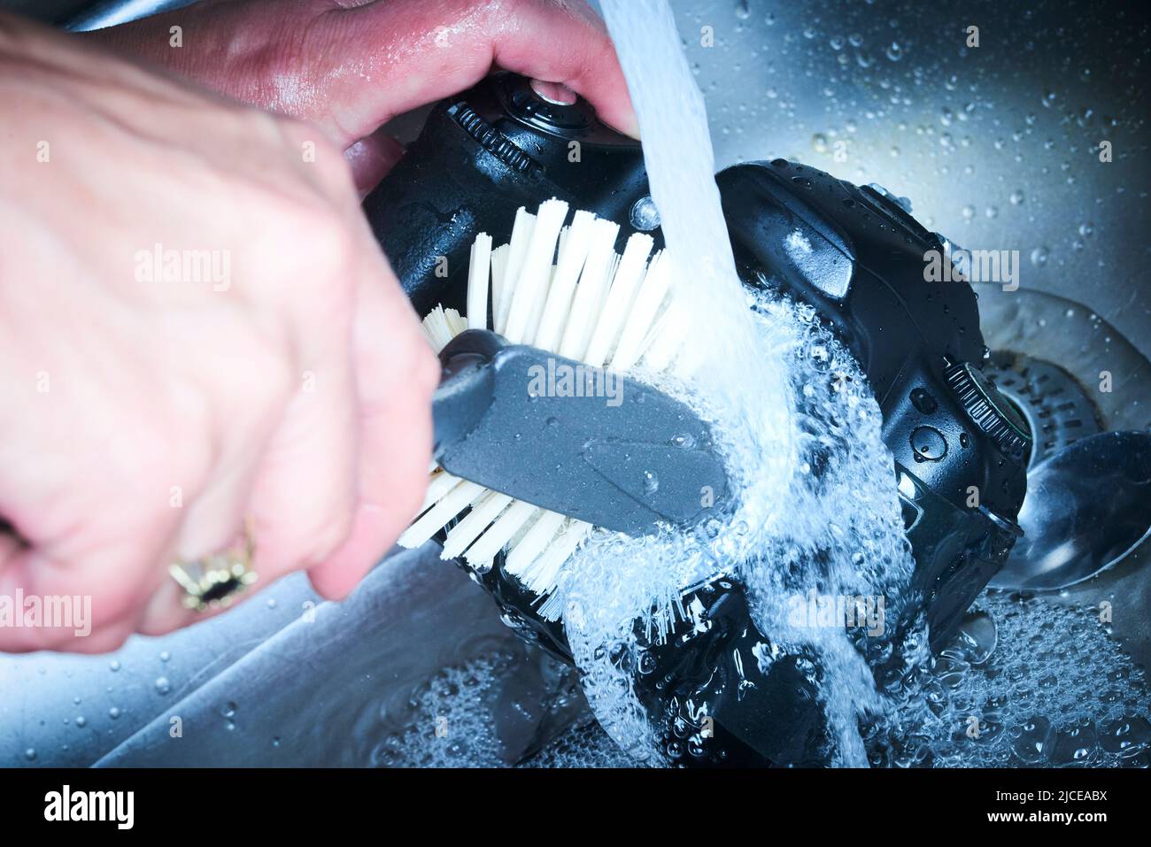 Weibliche Hände waschen dslr-Kamera als schmutziges Geschirr fließendes Wasser in der Spüle. Verrückter Fotograf reinigt den Kamerabild-Sensor schlecht mit Wasser Stockfoto