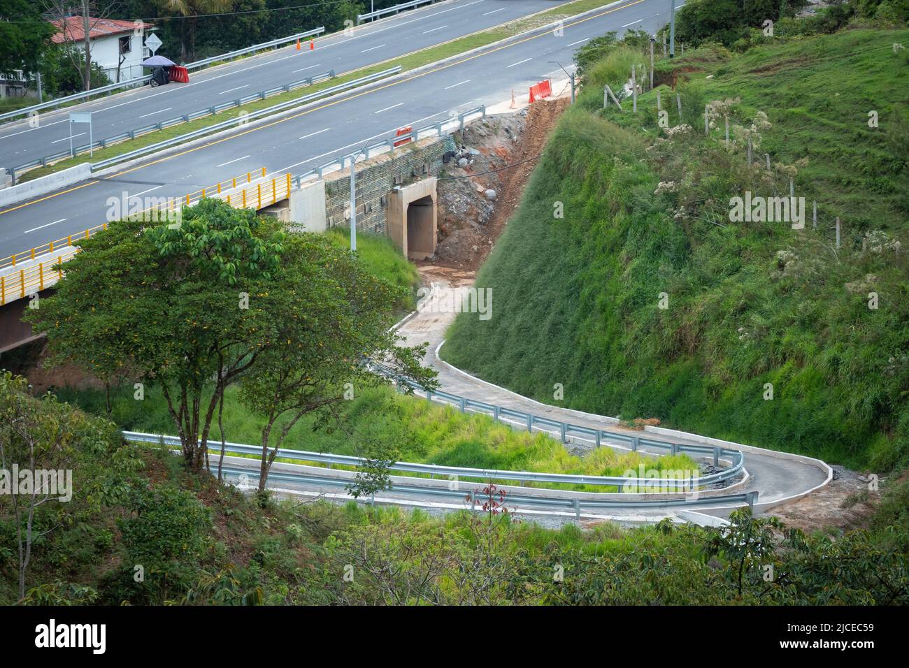 Enge Straße unter einer Brücke, an der Autos vorbei fahren und ein Tunnel im Bau mit viel Schlamm Stockfoto