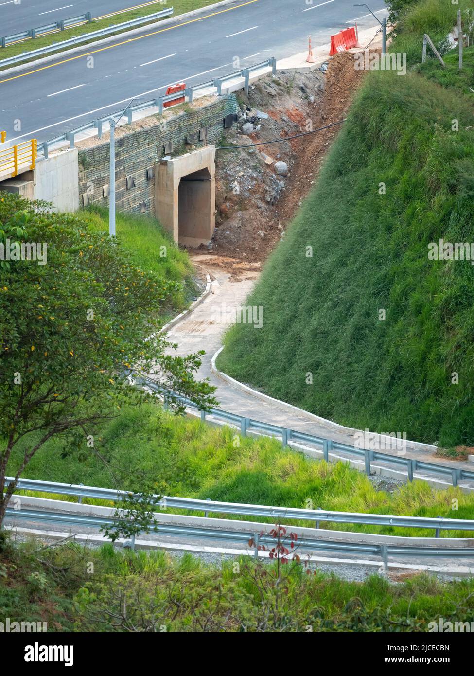 Enge Straße unter einer Brücke, an der Autos vorbei fahren und ein Tunnel im Bau mit viel Schlamm Stockfoto